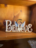 Decorative sign with angel and 'BELIEVE' letters on a wooden background- off white in color with gold glitter accents