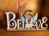 Decorative sign with angel and 'BELIEVE' letters on a wooden background- off white in color with gold glitter accents