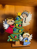 Decorative hand-painted shelf sitter with three angel figures and a Christmas tree on a wooden base.