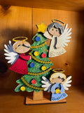 Decorative hand-painted shelf sitter with three angel figures and a Christmas tree on a wooden base.