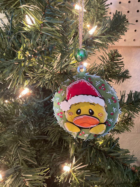 Christmas ornament with a duck wearing a Santa hat on a decorated wreath.