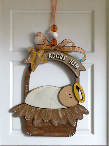 Baby Jesus in a manger with bronze ribbons and beads hanging on a door